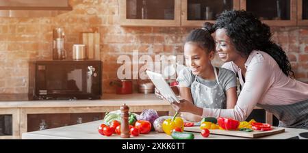 Maman et sa fille la lecture sur tablette Recette cuisine à Banque D'Images