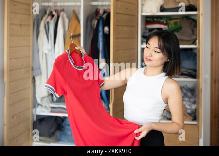 Heureuse jeune fille asiatique essayant de choisir une robe debout par garde-robe Banque D'Images