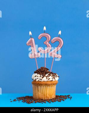 Bougie numéro 132 - carte d'anniversaire avec cupcake sur fond bleu Banque D'Images