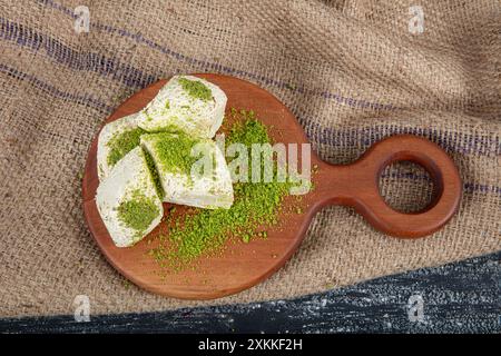 Pistache halva (Halvah). Halva avec des pistaches sur une table en bois rustique. Gros plan d'une assiette en bois avec halva de pistache turque traditionnelle et tranches Banque D'Images