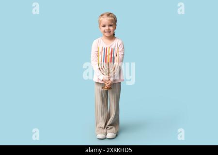 Jolie petite fille heureuse avec menorah sur fond bleu. Célébration Hanukkah Banque D'Images