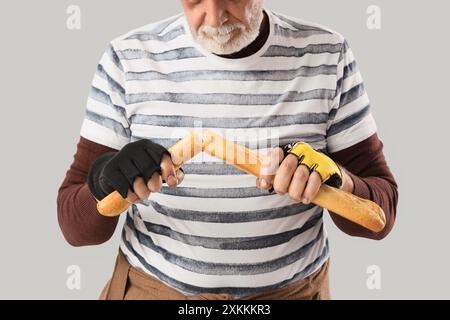 Homme sans-abri mature avec baguette sur fond clair, gros plan Banque D'Images