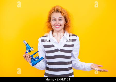 Une femme professeur de biologie scolaire tient un microscope. Femme professeur de biologie. Retour à l'école. Professeur avec microscope isolé sur jaune. Sciences biologiques Banque D'Images