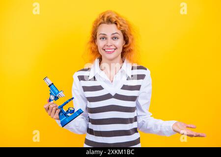 Une femme professeur de biologie scolaire tient un microscope. Femme professeur de biologie. Retour à l'école. Professeur avec microscope isolé sur jaune. Sciences biologiques Banque D'Images
