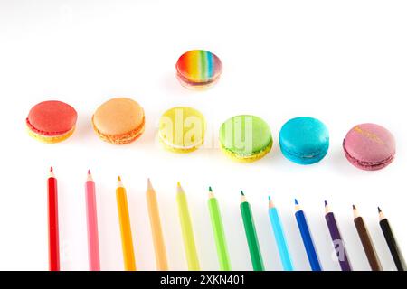 Un macaron arc-en-ciel vibrant entouré d'un ensemble de crayons de couleur disposés dans un motif circulaire sur un fond blanc. Banque D'Images