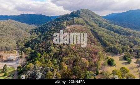 Photographie aérienne par drone de lignes de transmission passant au-dessus d'une grande colline dans les arbres dans la région des Snowy Mountains de Nouvelle-Galles du Sud, Australie. Banque D'Images