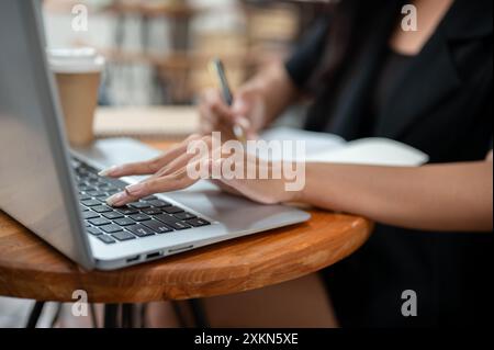 Une image recadrée d'une femme d'affaires asiatique travaillant à distance depuis un café dans la ville, travaillant sur son ordinateur portable, tapant sur le clavier de l'ordinateur portable et prenant non Banque D'Images