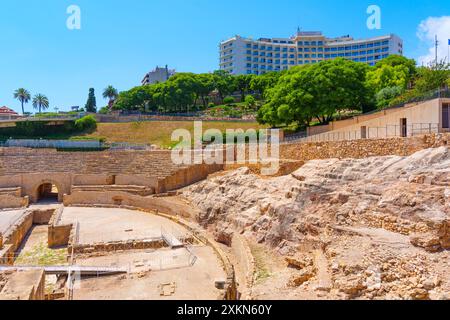 Tarragone, Espagne - 15 juillet 2024 : des ruines d'amphithéâtre avec des hôtels et des palmiers en arrière-plan à Tarragone, Espagne. Banque D'Images