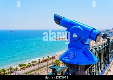 Tarragone, Espagne - 15 juillet 2024 : télescope bleu surplombant la mer avec navire lointain et la côte à Tarragone, Espagne. Banque D'Images