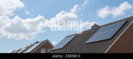 Cellules solaires bleues ou panneaux solaires sur les toits des maisons dans une rangée reflétant le ciel nuageux bleu. Concept d'énergie verte durable Banque D'Images