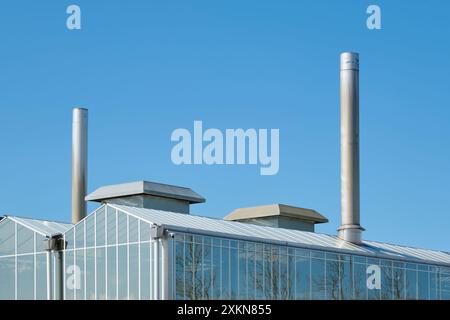 Toit d'une serre industrielle avec cheminées contre un ciel bleu ensoleillé. Image avec espace de copie Banque D'Images