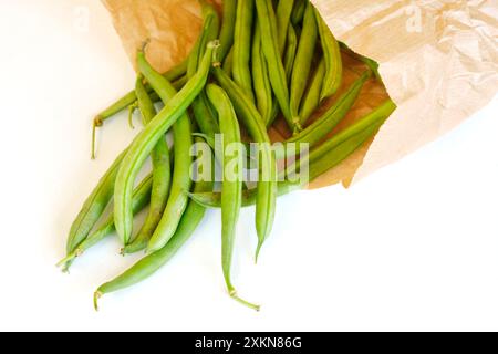 Gros plan de gousses de haricots verts mûrs biologiques dans un sac écologique en papier brun sur fond blanc. Concept d'environnement zéro déchet. Banque D'Images