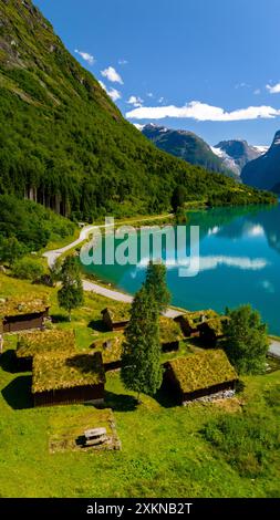 Une vue pittoresque sur les cottages traditionnels aux toits d'herbe nichés au bord d'un fjord norvégien tranquille, entouré de collines verdoyantes et d'un ciel bleu clair. Lovatnet lac Lodal vallée Norvège Banque D'Images