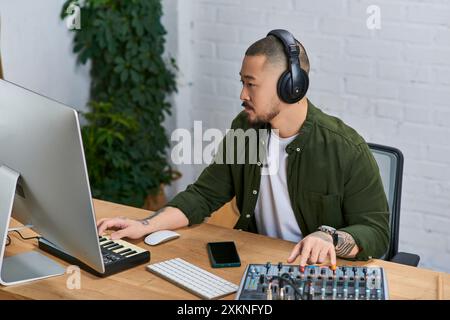 Un bel homme asiatique, portant des écouteurs, travaille sur un projet musical dans son studio. Banque D'Images