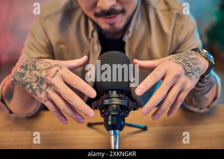 Gros plan des mains d'un homme, lourdement tatouées, tenant un microphone dans un studio d'enregistrement. Banque D'Images