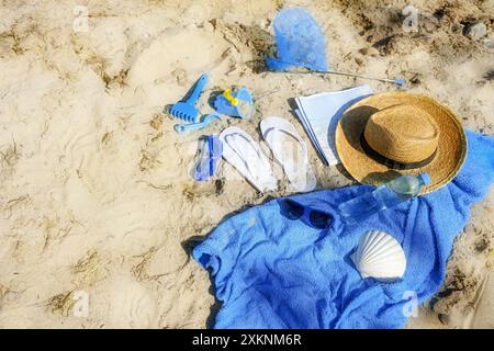 Lieu familial à la plage avec serviette bleue, tongs, jouets, coquille et chapeau de paille, vacances d'été à la mer, vu d'en haut, espace copie, sélectionné Banque D'Images