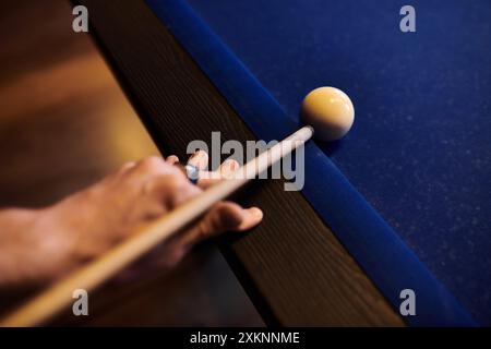 Gros plan d'une main tenant une queue de billard, visant une boule blanche sur la table en feutre. Banque D'Images