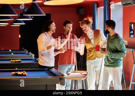 Les amis se tiennent autour d'une table de billard, boissons à la main, dans un cadre décontracté. Banque D'Images