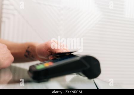 Gros plan recadré d'un client méconnaissable payant avec une carte de crédit sans contact avec technologie NFC. Gros plan client payant la facture en main par Banque D'Images