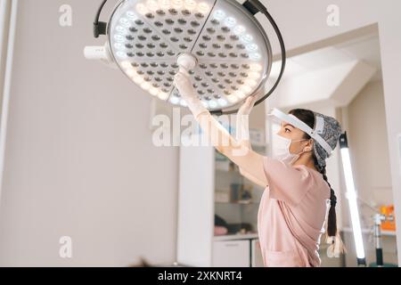 Médecin féminin portant l'uniforme médical ajustant la préparation de la lumière effectuant l'opération à l'hôpital. Chirurgien ajustant la lampe chirurgicale avant le médical Banque D'Images