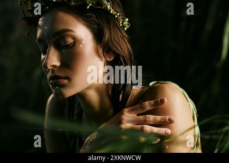 Une femme avec une couronne de fleurs pose dans l'ombre d'un marais, entourée d'une végétation luxuriante. Banque D'Images