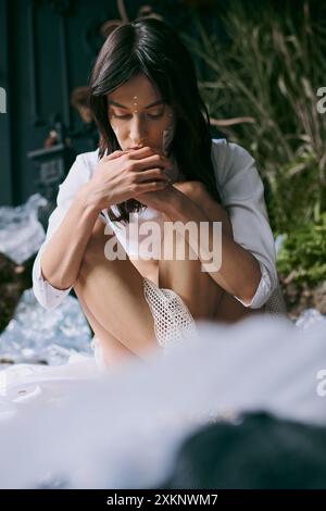 Une jeune femme pose soigneusement dans une robe blanche au milieu d'un marais rempli de déchets plastiques. Banque D'Images