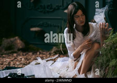 Une femme vêtue de vêtements esthétiques pose au milieu d'un marais rempli de déchets plastiques. Banque D'Images