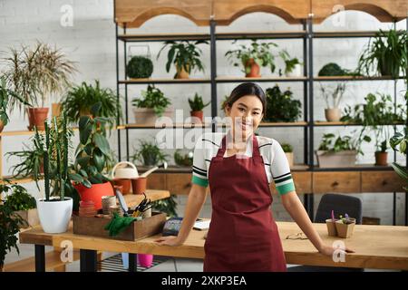 Une jeune femme asiatique, propriétaire d’un magasin d’usine, sourit chaleureusement en travaillant dans son magasin, entourée d’une verdure vibrante. Banque D'Images