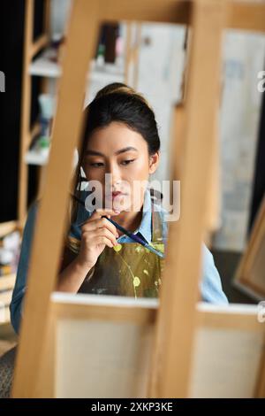 Une jeune artiste asiatique, vêtue d’un tablier, peint soigneusement dans son atelier. Banque D'Images
