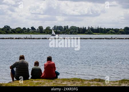 Arnis, Allemagne. 24 juillet 2024. Deux adultes et un enfant sont assis sur le rivage au soleil et regardent sur le Schlei. Crédit : Frank Molter/dpa/Alamy Live News Banque D'Images