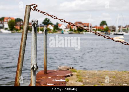 Sundsacker, Allemagne. 24 juillet 2024. Une chaîne pend sur le rivage. Le ferry broyeur qui relie la petite ville d'Arnis (district de Schleswig-Flensburg) à la rive sud du Schlei est hors service depuis deux ans. Selon le maire Matthiesen, la réparation du ferry coûterait 350 000 euros. Crédit : Frank Molter/dpa/Alamy Live News Banque D'Images