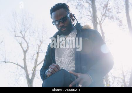 Homme noir dans debout dans le parc tient et ouvre un sac de fanny dans sa main, il y a une atmosphère de lumière du soleil sur la scène, porte des dreadlocks et être Banque D'Images