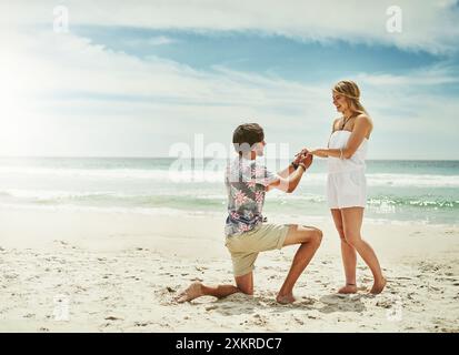 Mariage, proposition et couple avec amour à la plage pour les fiançailles, la surprise et le bonheur en vacances. Ciel bleu, vagues et homme avec demander sur genou pour Banque D'Images