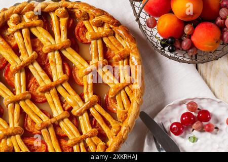 Tarte à l'abricot décorée d'ornement de pâte et d'un panier en métal avec des fruits et des baies sur un fond clair. Style rustique, mise au point sélective. Banque D'Images