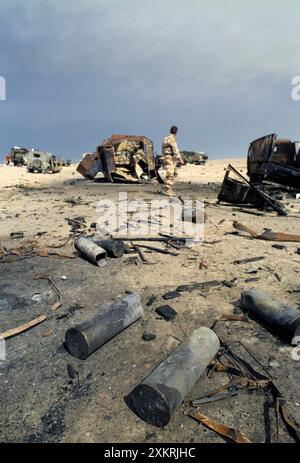 Première Guerre du Golfe : 4 mars 1991 Un soldat britannique explore parmi les épaves de véhicules militaires abandonnés par l'armée irakienne sur la route 801, la route d'Um Qasr, au nord de Koweït City. C'était l'un des convois militaires irakiens, fuyant vers l'Irak, qui a été attaqué et détruit environ une semaine auparavant par l'USAF. Banque D'Images