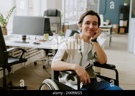 Portrait de souriant spécialiste INFORMATIQUE caucasien avec handicap regardant la caméra tandis que sa tête basée sur la main, il est au bureau d'une entreprise INFORMATIQUE moderne haut de gamme Banque D'Images