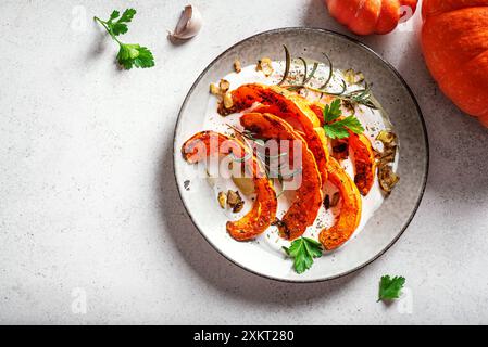 Citrouille rôtie avec yaourt grec, ail et herbes sur table blanche, vue de dessus, espace copie. Recette chaude de salade de citrouille épicée d'hiver avec chèvre labneh molle Banque D'Images