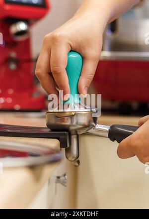 Barista des mains, bourrage de la rondelle de café moulu espresso pressant dans le café. intérieur, gros plan, vue latérale, verticale Banque D'Images