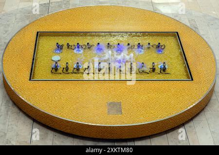 Fontaine rectangulaire sur un piédestal circulaire de carreaux de mosaïque jaune, posée sur un sol en dalle de pierre. Banque D'Images