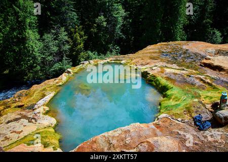 Piscine naturelle de source chaude dans la forêt avec sandales et bouteille d'eau au niveau des yeux Banque D'Images