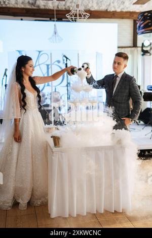 lors d'un banquet, les jeunes mariés versent du champagne dans une pile de verres pour les invités Banque D'Images