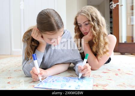 Deux filles faisant maths mathématiques allongées sur le sol écrivant sur un tableau blanc avec des stylos algèbre fractions mathématiques soeurs mathématiques éducation filles en STIM Banque D'Images