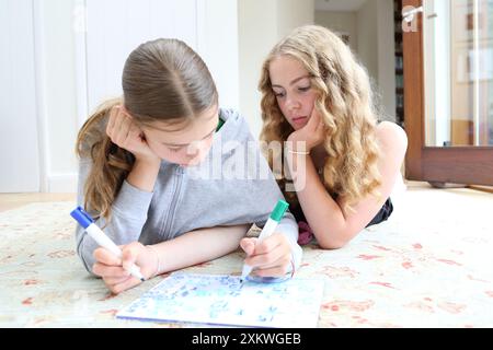 Deux filles faisant maths mathématiques allongées sur le sol écrivant sur un tableau blanc avec des stylos algèbre fractions mathématiques soeurs mathématiques éducation filles en STIM Banque D'Images