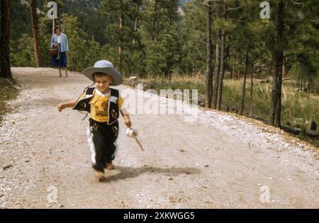 YoungBoy habillé comme un cow-boy court devant sa mère dans les Black Hills du Dakota du Sud, années 1950, USA Banque D'Images