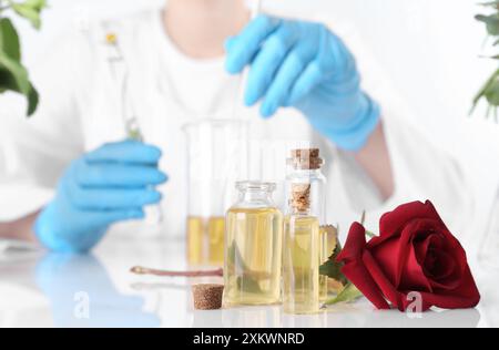 Produit d'aromathérapie. Scientifique développant des huiles essentielles à table blanche en laboratoire, focus sur les bouteilles et la rose Banque D'Images