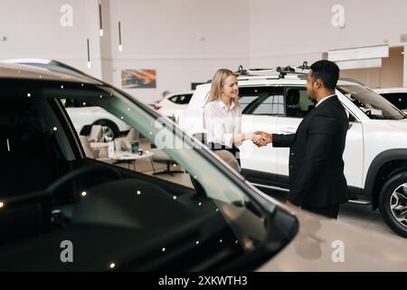 Portrait de la femme heureuse cliente blonde remerciant le concessionnaire afro-américain masculin portant costume pour aider à choisir la voiture à acheter dans le centre de concession. Banque D'Images