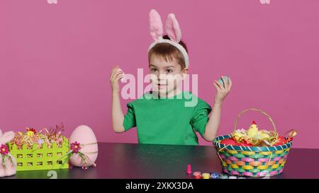 Enfant mignon souriant jouant un coup d'œil à un jeu de boo avec des œufs colorés peints, s'amusant avec des décorations de pâques et des arrangements sur la caméra. Garçon joyeux enthousiaste étant excité par les vacances. Caméra A. Banque D'Images