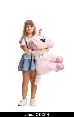 Portrait pleine longueur d'une petite fille tenant un grand jouet licorne isolé sur fond blanc Banque D'Images