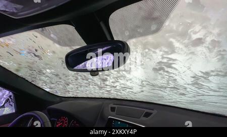 Eau savonneuse sur le pare-brise d'une voiture à l'intérieur d'un lave-auto automatisé. Banque D'Images