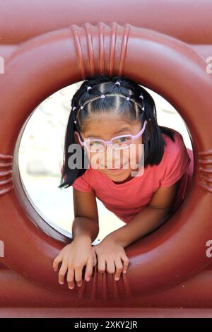 Fille brune latine de 5 ans joue dans le parc de jeux loin des enfants dans la solitude pendant son week-end de vacances Banque D'Images